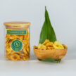 Hausgemachte Bananenchips mit Schweizer Salz Fleur des Alpes. In einer Verpackung aus Borosilikatglas. Und es ist noch eine Bambus Schale sowie ein grünes Blatt zu sehen.